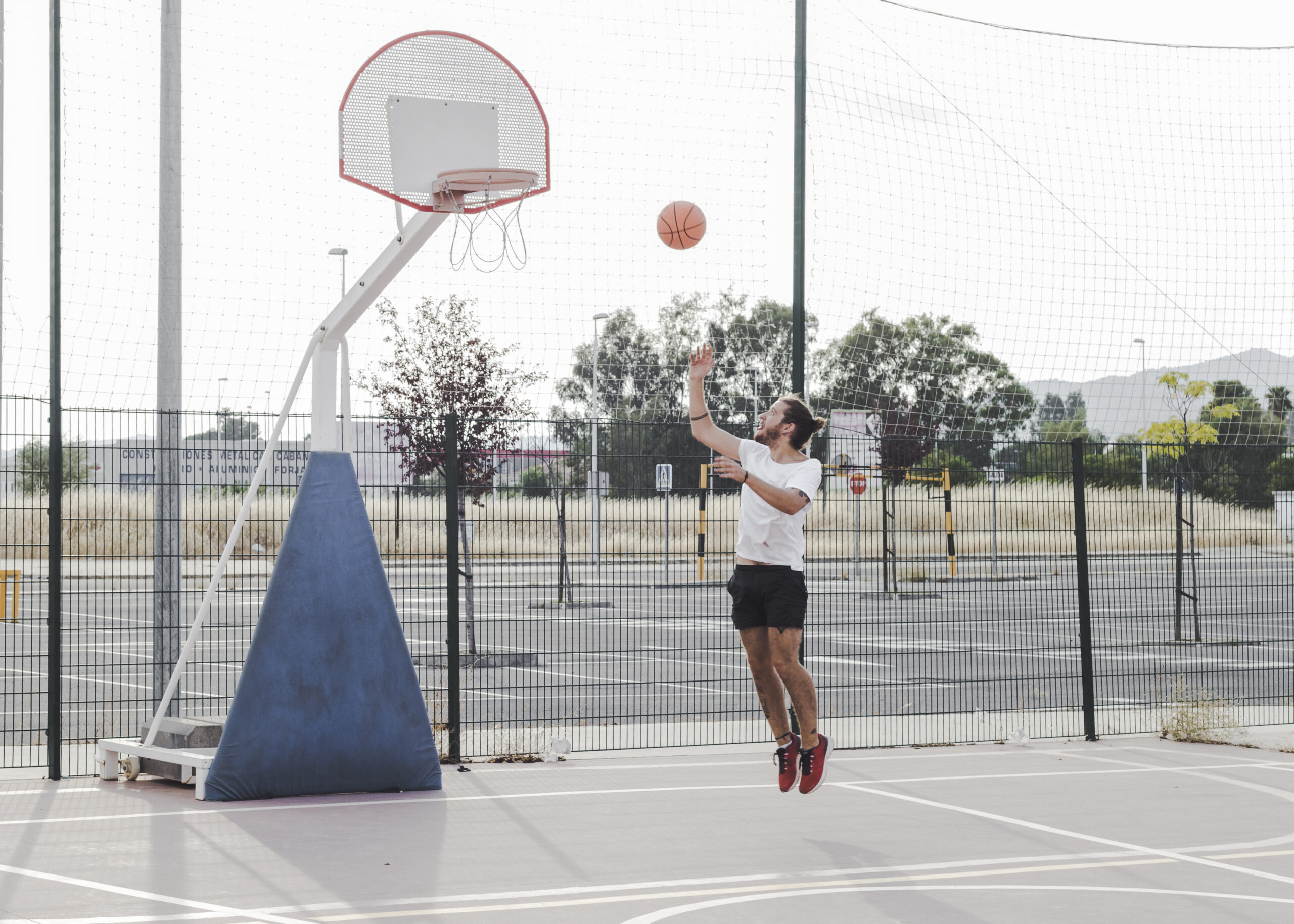 Basketball player jumping to shoot on an outdoor court enclosed by green welded mesh sports court fencing